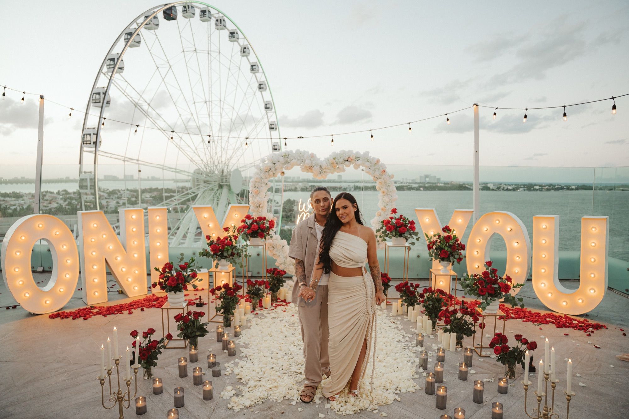 Propuesta Bespoke en rooftop con la pareja frente a las letras "ONLY YOU" a medida, arco de corazón floral y vista al mar