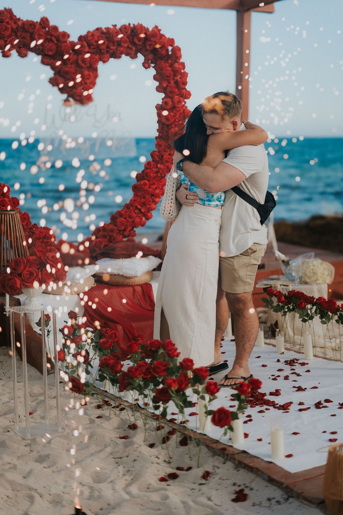 Romantic embrace on a secluded wooden deck surrounded by tropical greenery, capturing the intimacy of the just-engaged couple.