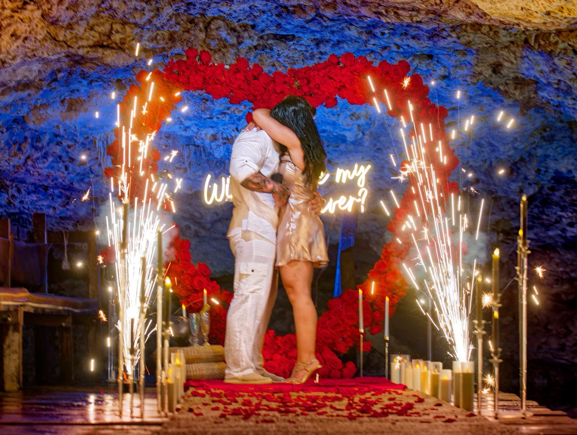 Propuesta íntima en cenote con la pareja abrazada dentro de un arco de corazón de rosas enmarcado por chisperos fríos