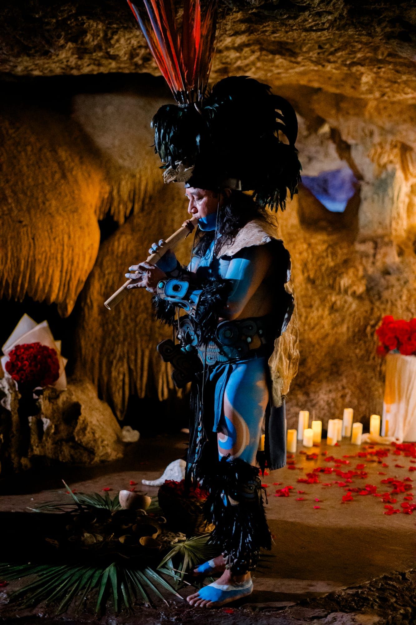 Músico de bendición maya interpretando en una cueva de cenote iluminada con velas en Riviera Maya, junto a un montaje de propuesta con rosas rojas.