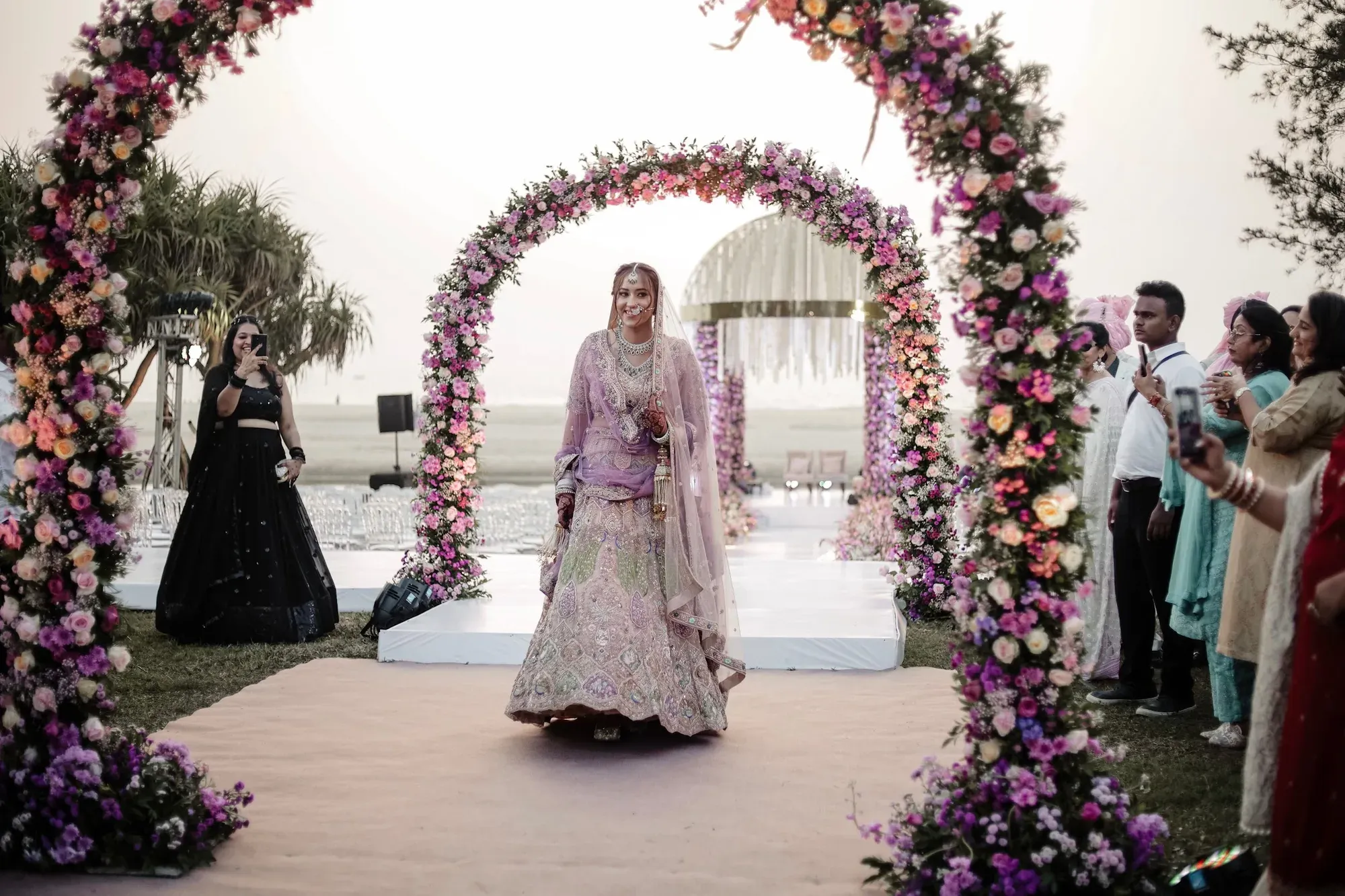 Bride walking toward a floral arch during the ceremony